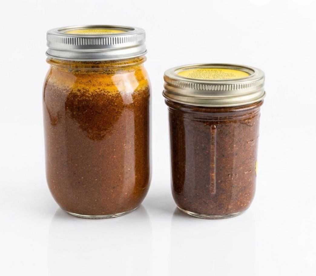 Wooden spoon lifting orange-brown sauce from a glass jar on a white background