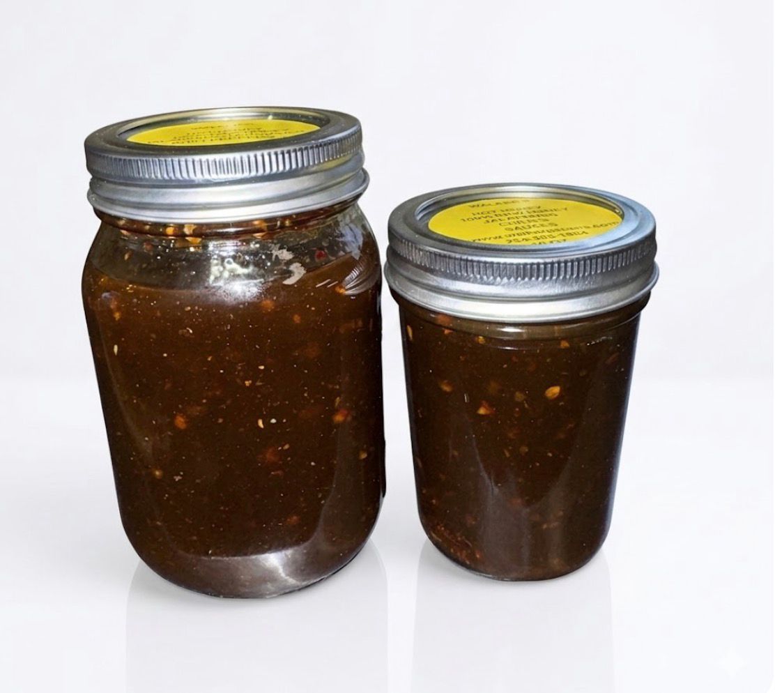 Jar of dark chili sauce with a wooden spoon dripping sauce above it, on a light background