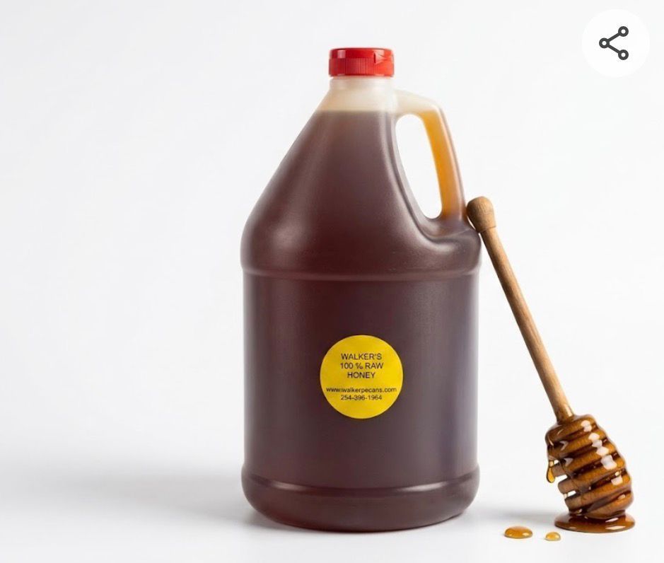 Plastic jug of dark syrup with red cap and honey dipper on a white background