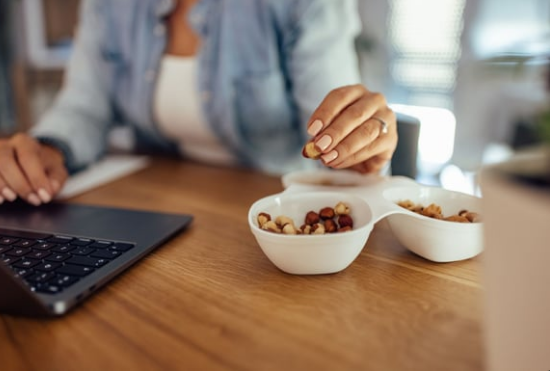Person working at a laptop and reaching for a snack bowl on a wooden desk