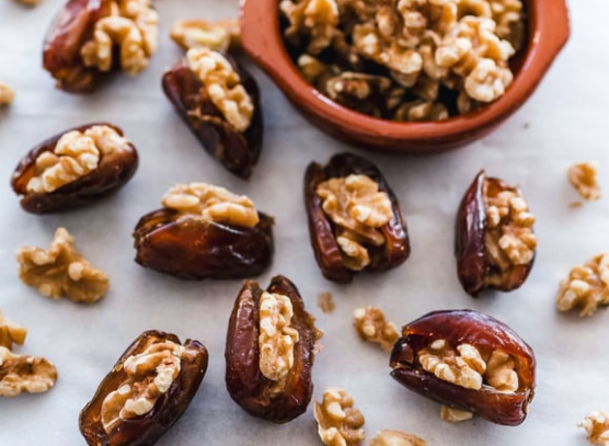 Walnuts in shells and halves scattered on a light surface, with a bowl of walnut halves nearby