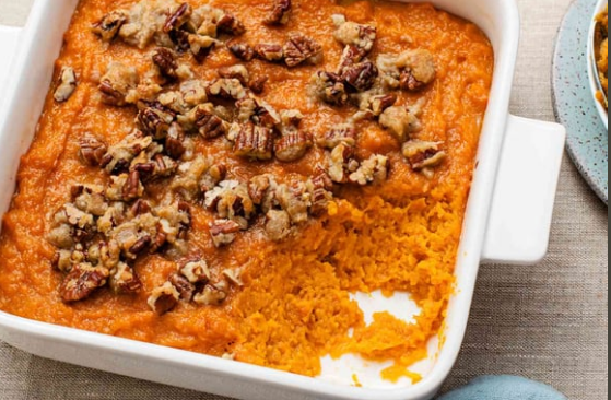 Orange sweet potato casserole topped with chopped nuts in a white baking dish