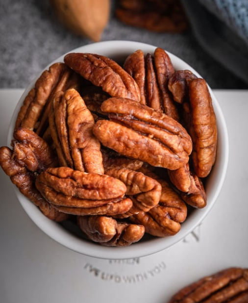 A bowl of pecans on a white plate, viewed from above.