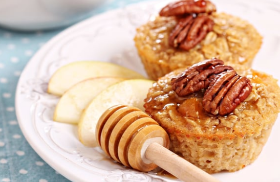 Muffins topped with pecans on a white plate with apple slices and honey drizzled beside them