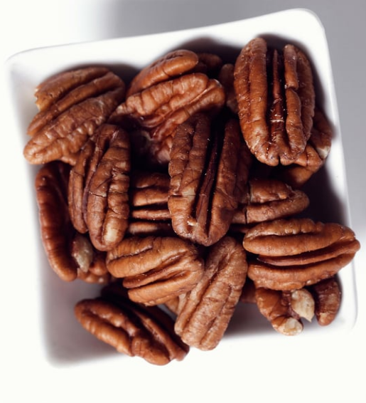 A white square bowl filled with brown pecan halves on a white background