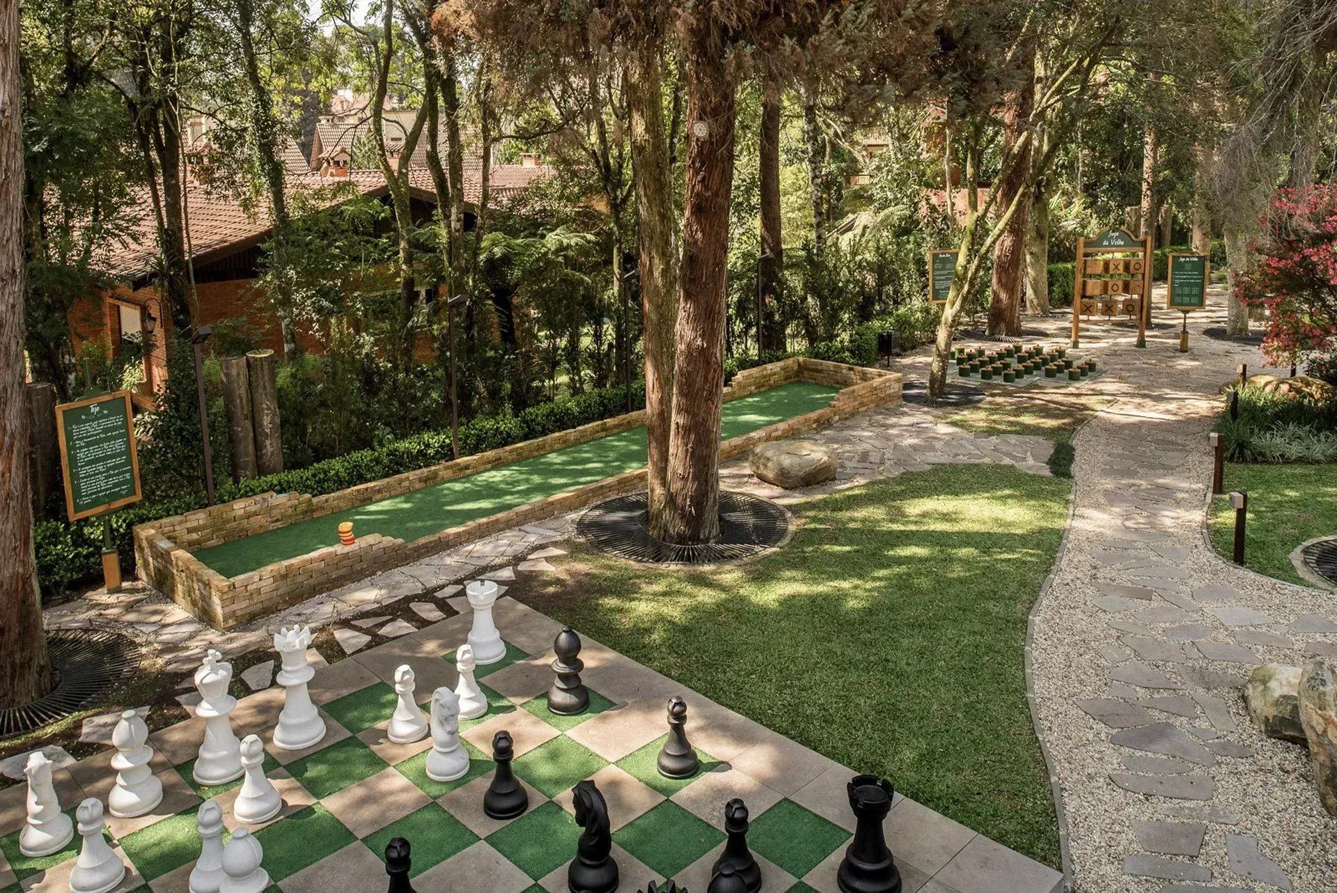 Tabuleiro de xadrez ao ar livre em um parque arborizado com bancos, caminhos e árvores grandes.