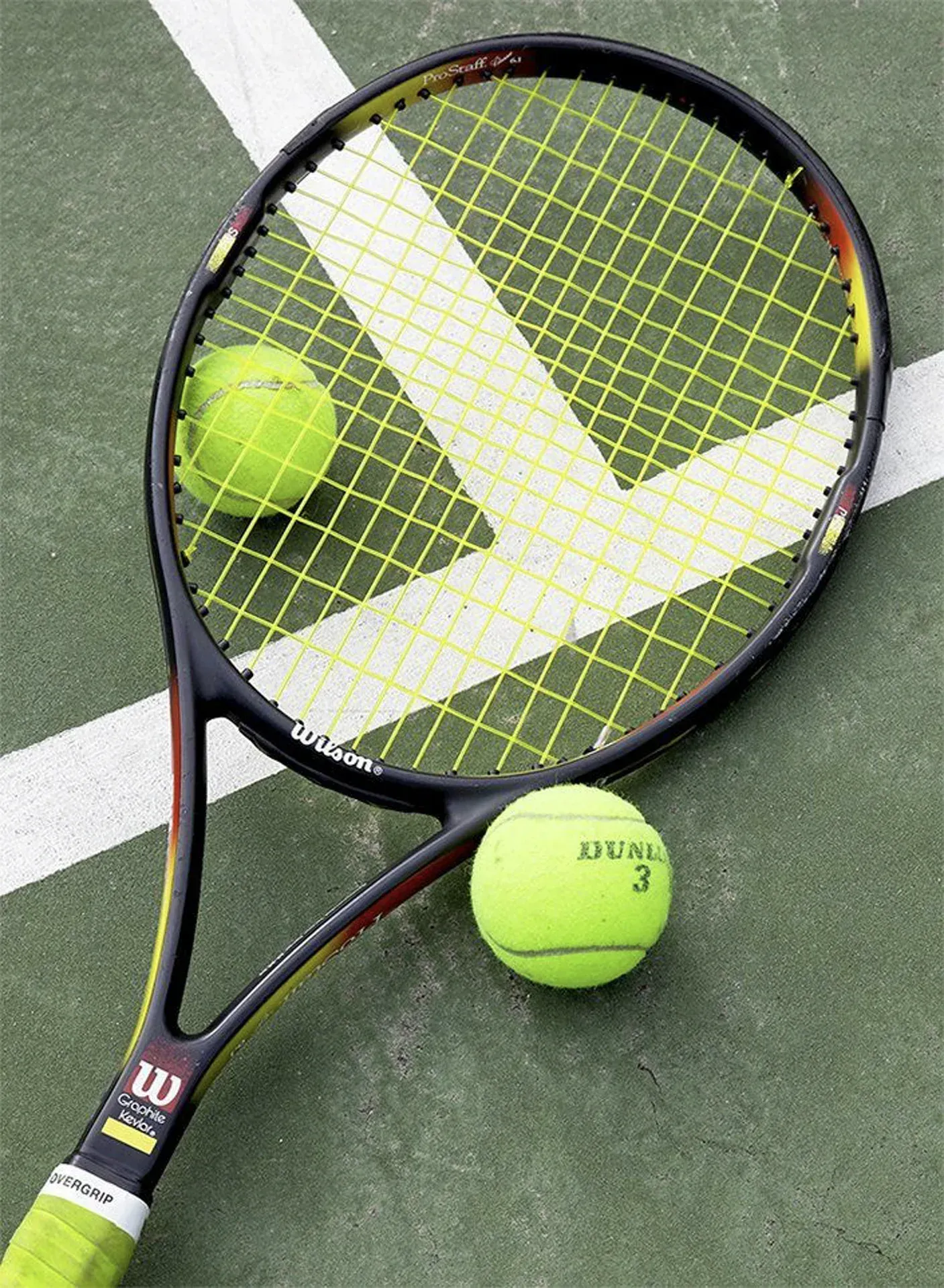 Raquete de tênis e duas bolas de tênis amarelas sobre uma quadra verde.