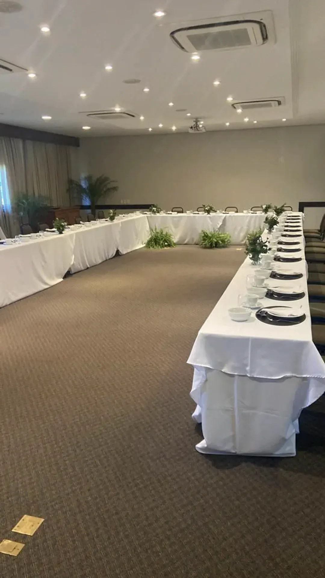 Mesa de banquete em formato de U disposta em uma sala de conferências com toalhas de mesa brancas e lugares marcados.