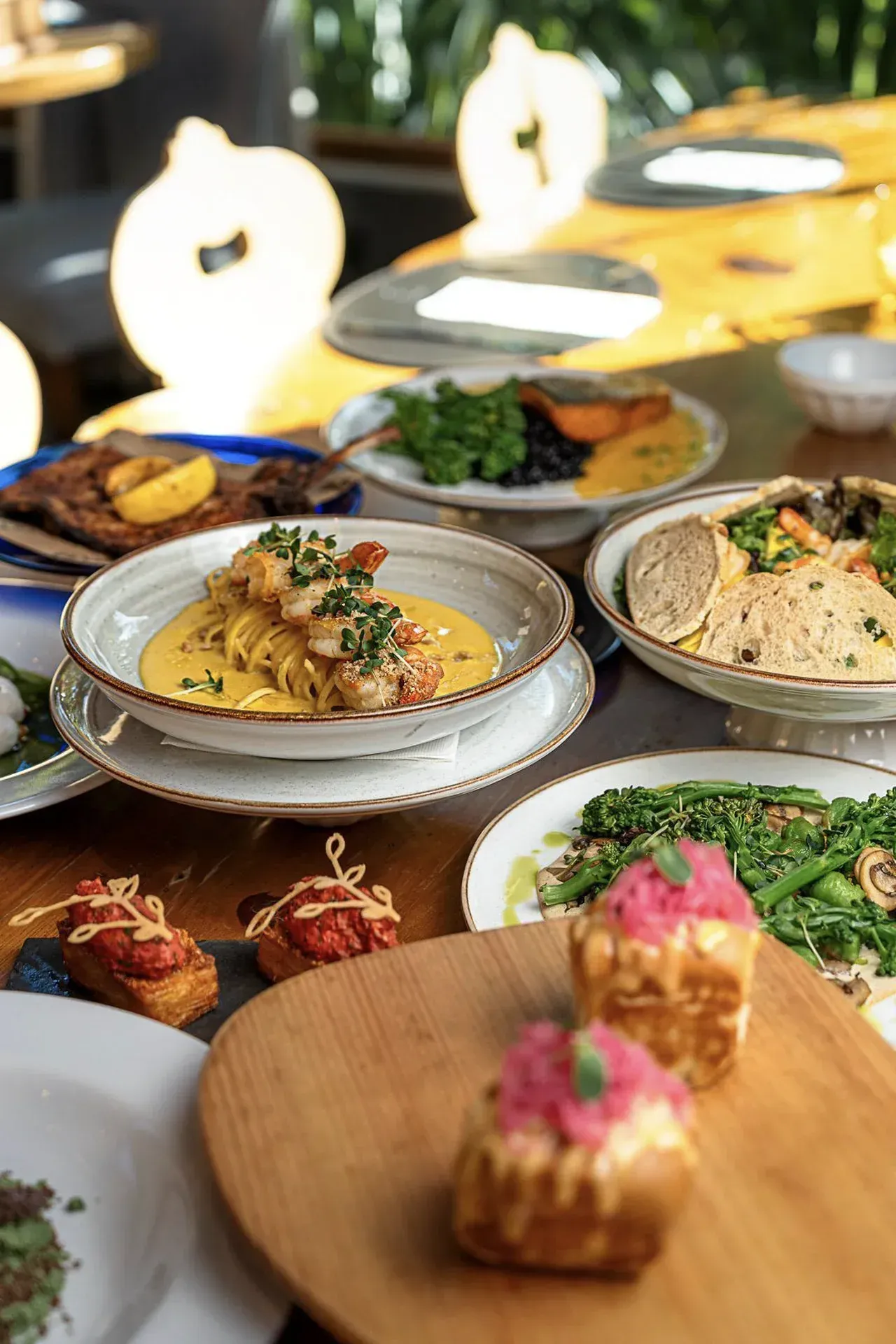 Mesa de buffet com diversos pratos e aperitivos sob uma iluminação externa aconchegante.