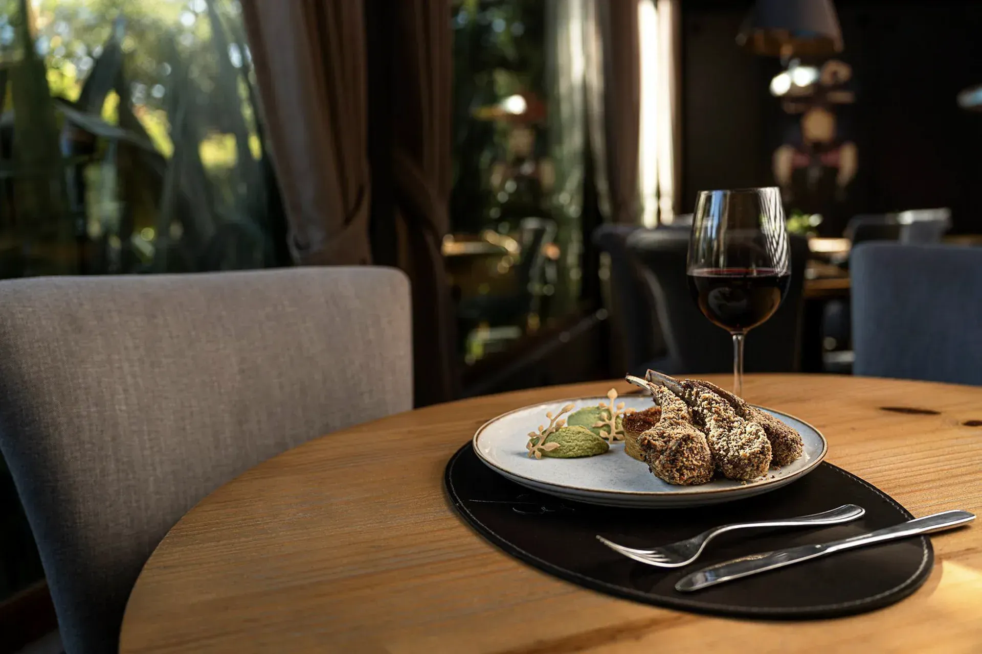 Mesa de restaurante com bife no prato, acompanhamento, taça de vinho e talheres sobre uma mesa de madeira.