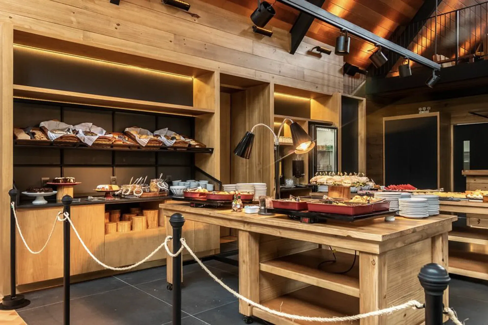 Mesa de buffet rústica com pão, pratos e travessas em uma sala de jantar aconchegante com painéis de madeira.