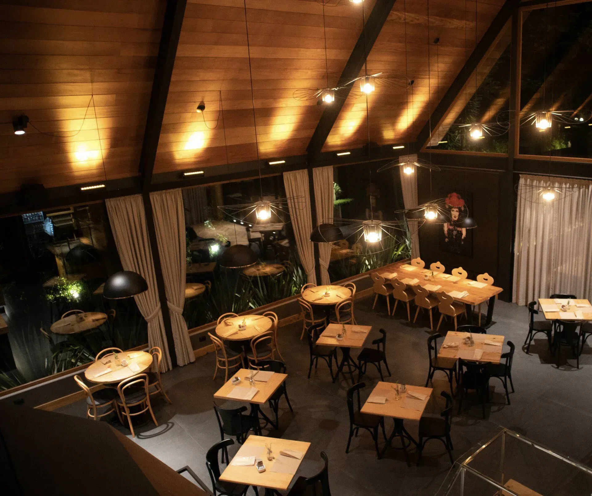 Restaurante aconchegante com iluminação suave, teto de madeira, mesas postas para refeições e janelas amplas.