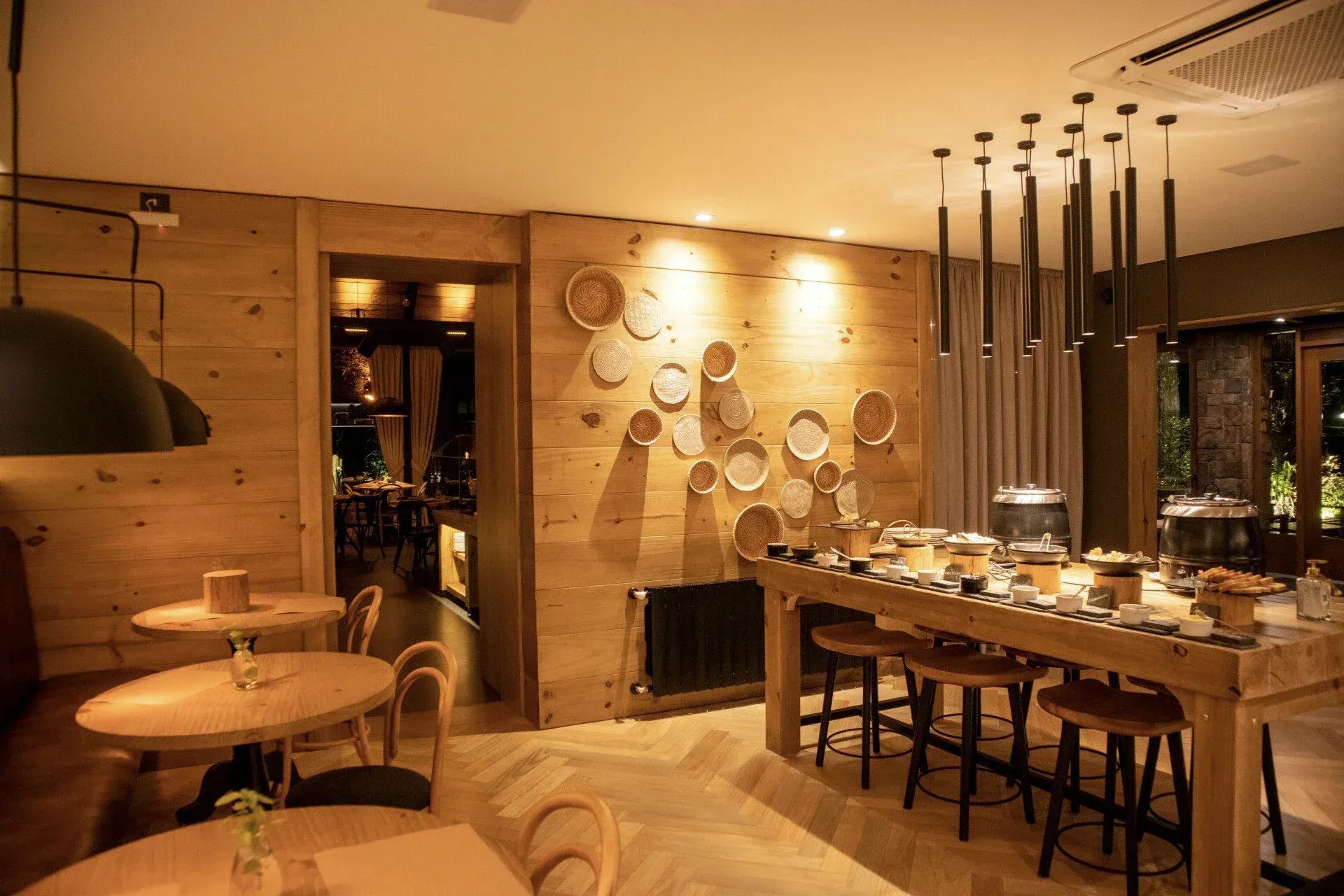 Sala de jantar aconchegante com painéis de madeira, iluminação quente, luminárias pendentes e uma longa mesa posta para refeições.