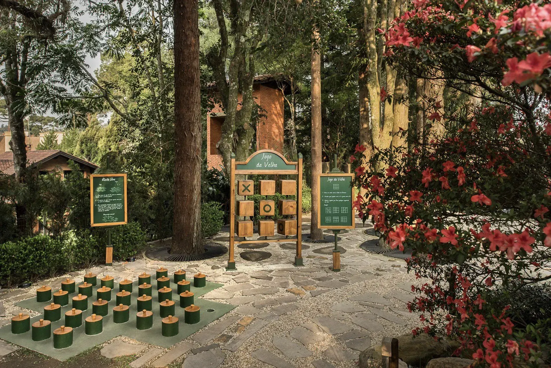 Jardim externo com placas de madeira e fileiras de pequenos vasos verdes entre árvores e flores.