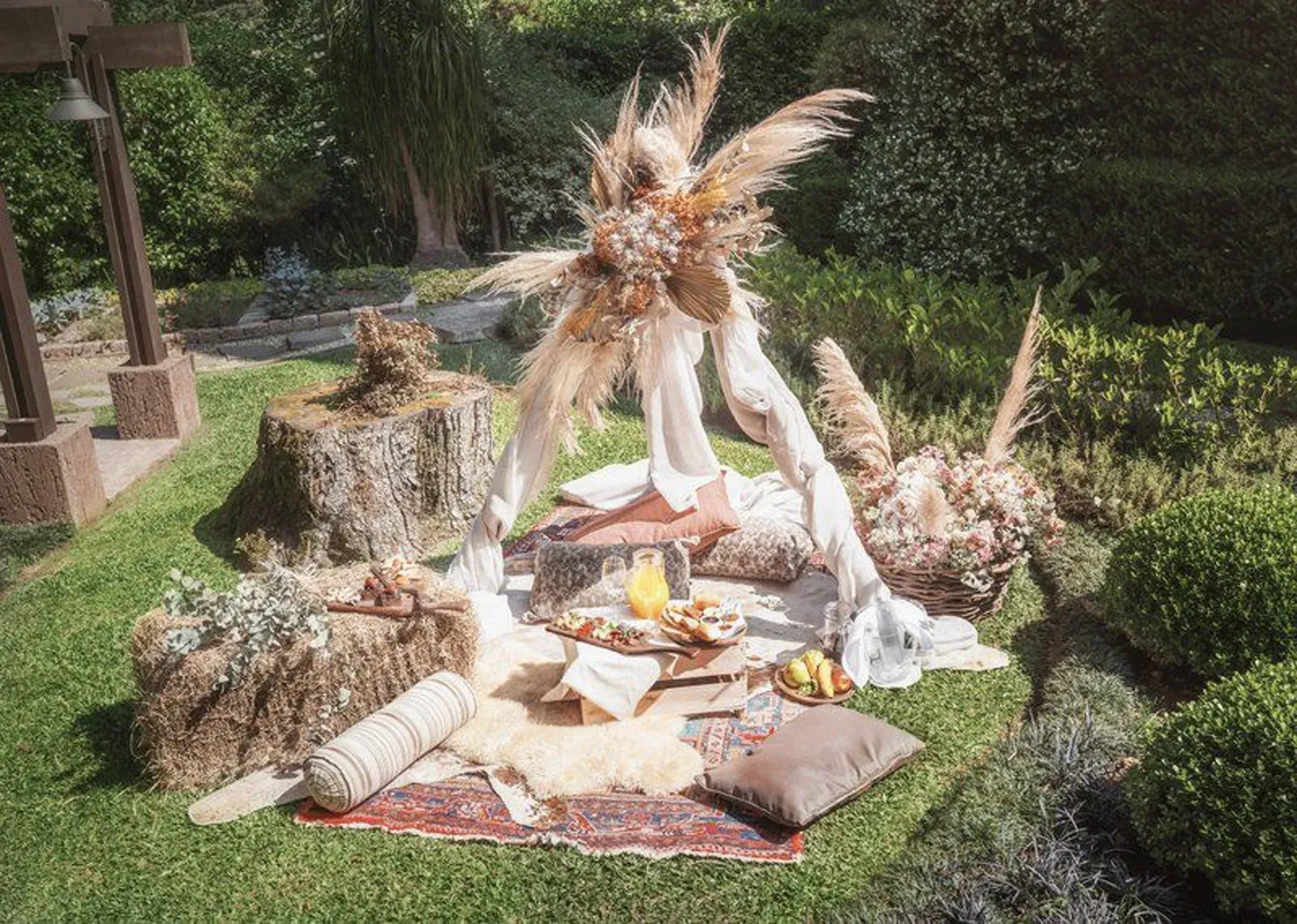 Duas esculturas fantásticas com chifres ao lado de uma mesa de piquenique estendida sobre uma manta em um jardim.