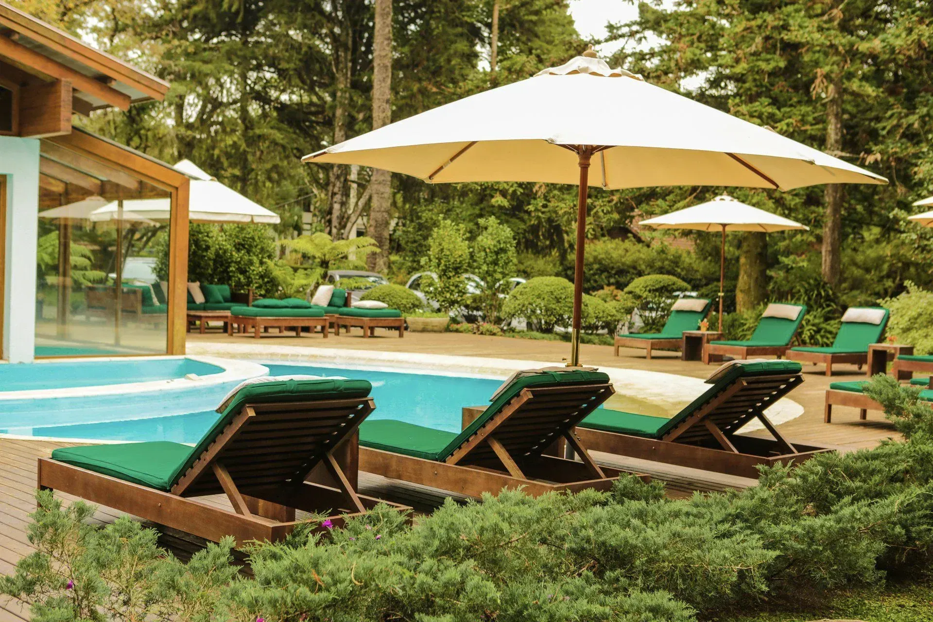 Resort à beira da piscina com espreguiçadeiras, guarda-sóis e vegetação tropical ao lado de uma villa moderna.