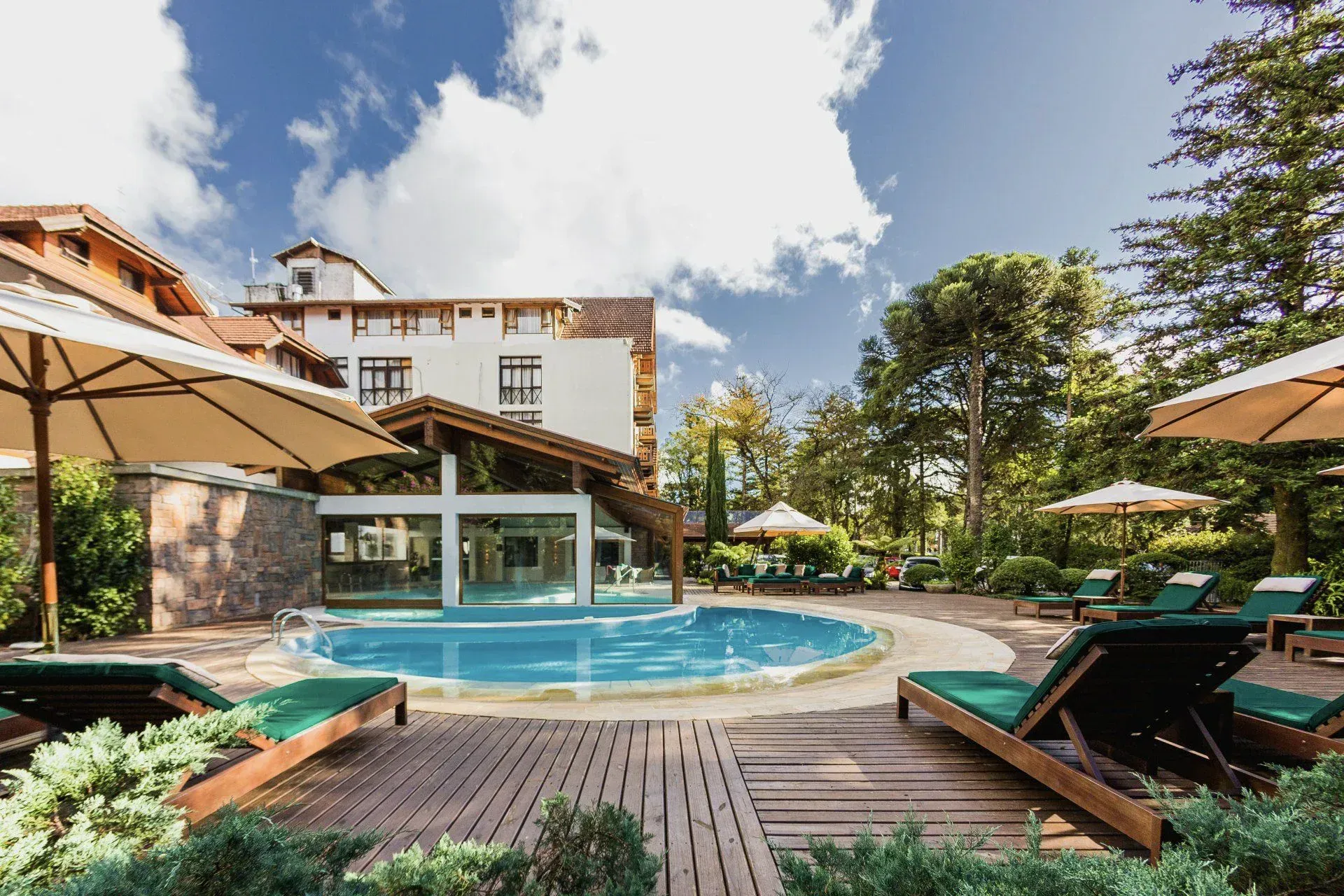 Piscina do resort com espreguiçadeiras e guarda-sóis em um jardim ensolarado no pátio.