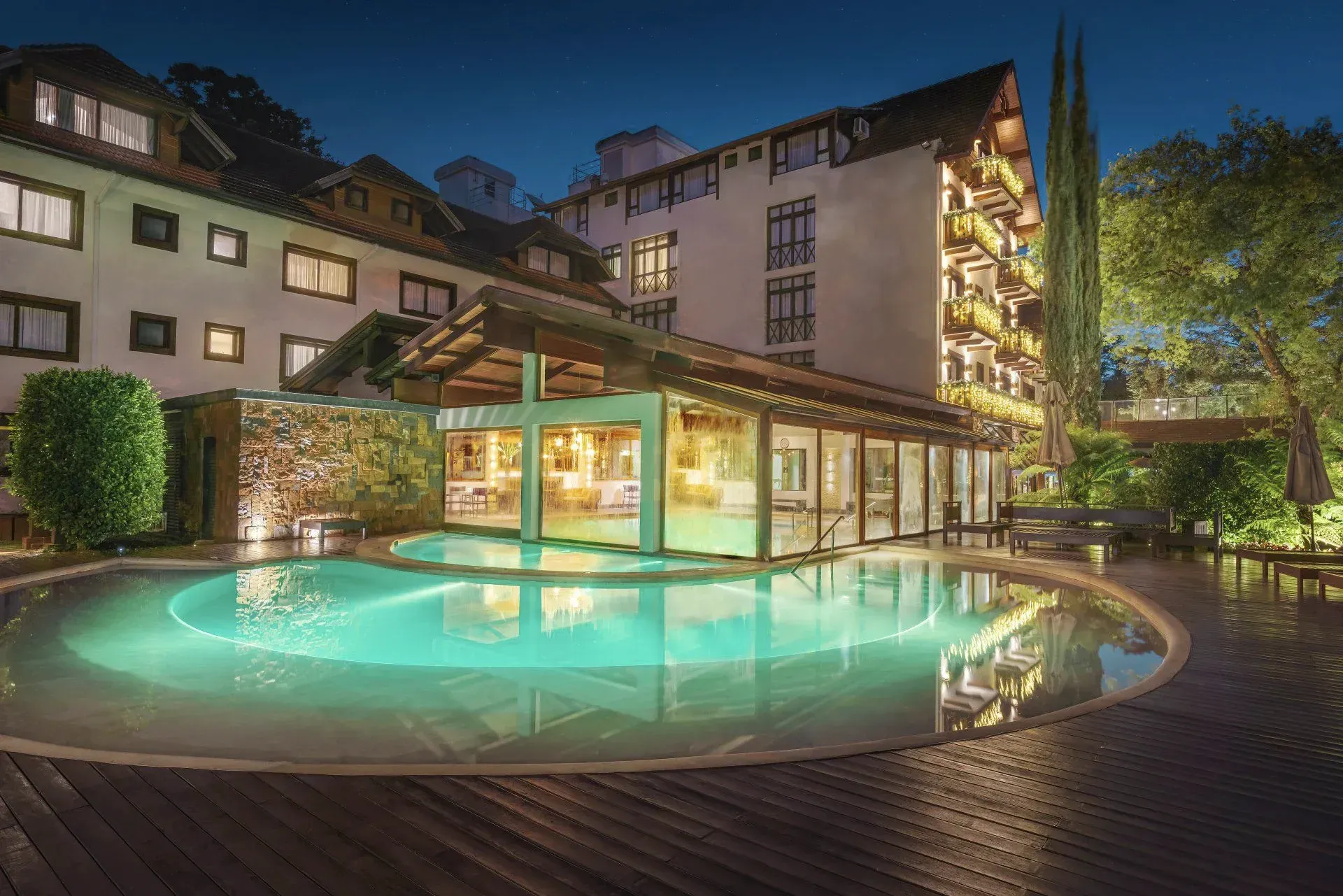 Pátio do hotel com piscina externa iluminada à noite e varandas iluminadas ao fundo.