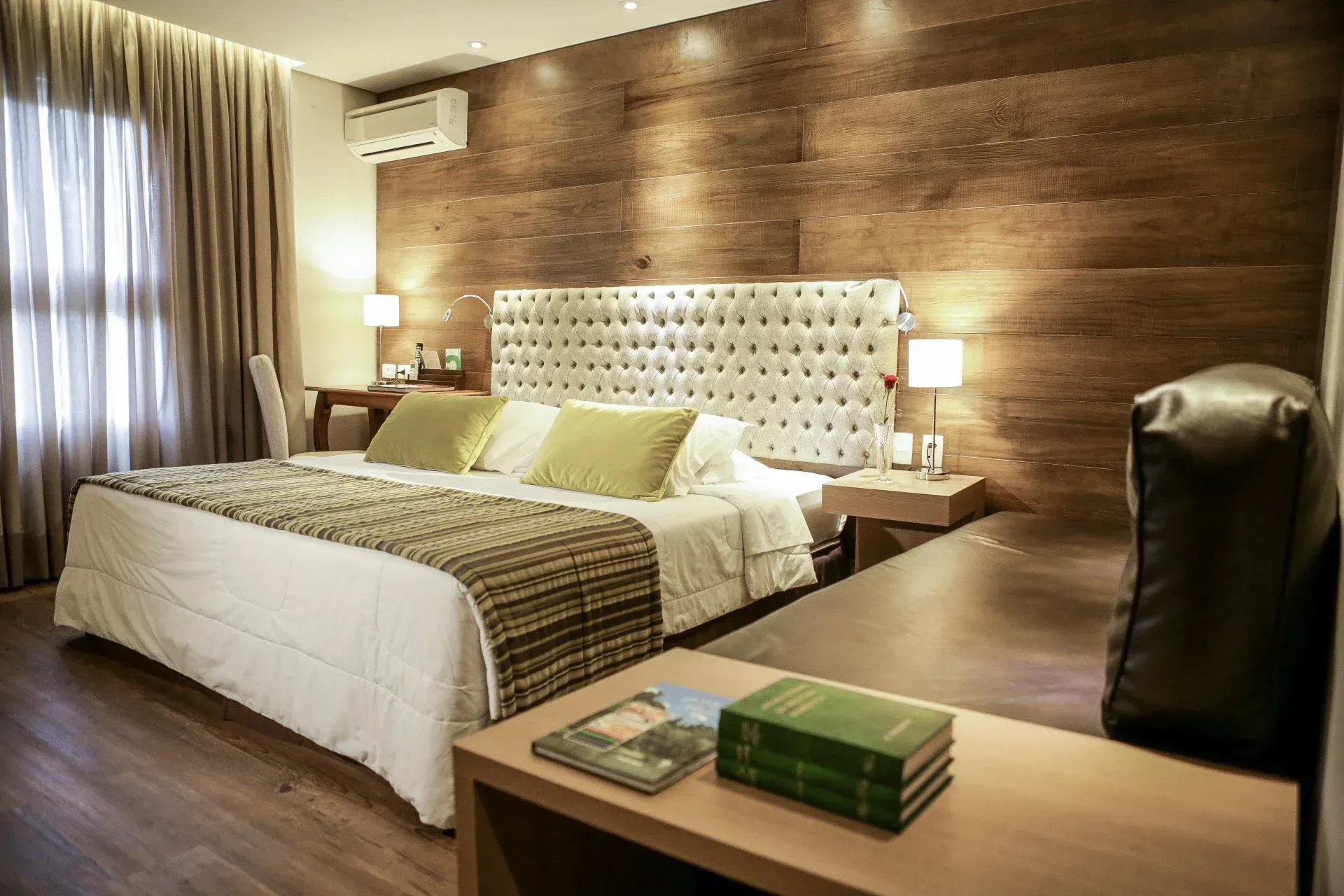Quarto de hotel moderno com cama grande, parede revestida de madeira e iluminação suave.