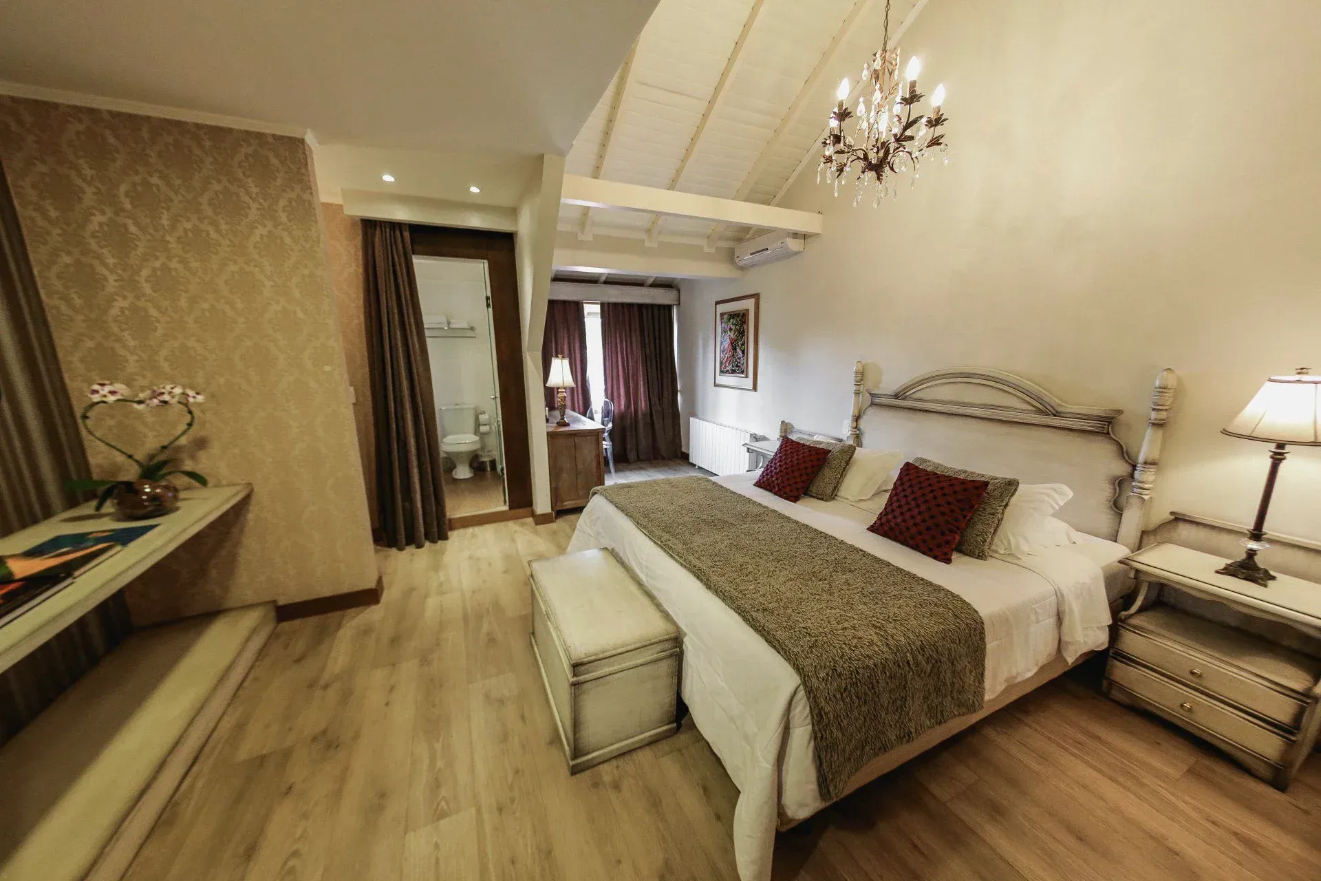 Quarto de hotel elegante com cama king-size, lustre e decoração em tons de bege aconchegante.
