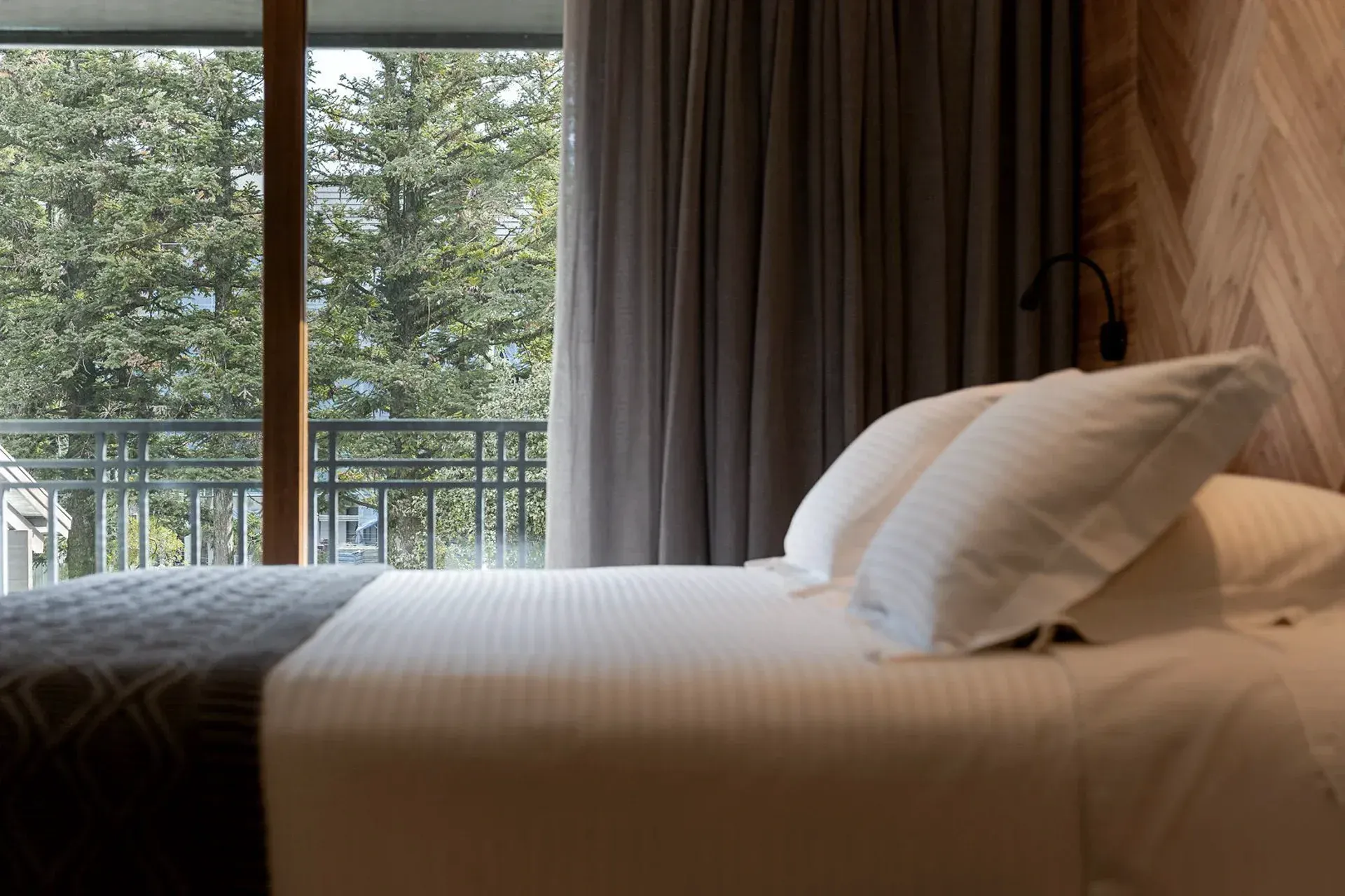 Quarto de hotel moderno com cama bem arrumada e varanda com vista para as árvores.