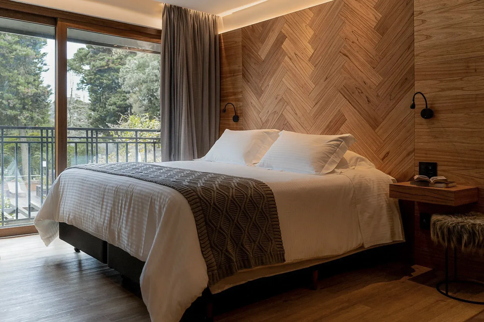 Quarto aconchegante com cama grande, parede com detalhes em madeira e portas de vidro deslizantes que dão para uma varanda.