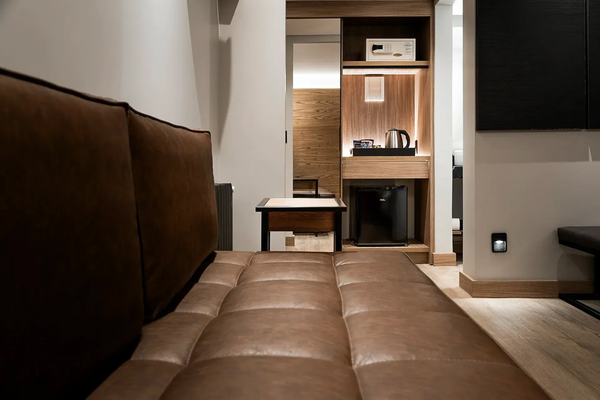 Sala de estar aconchegante com um sofá de couro marrom em frente a uma parede de TV com painéis de madeira e hall de entrada.