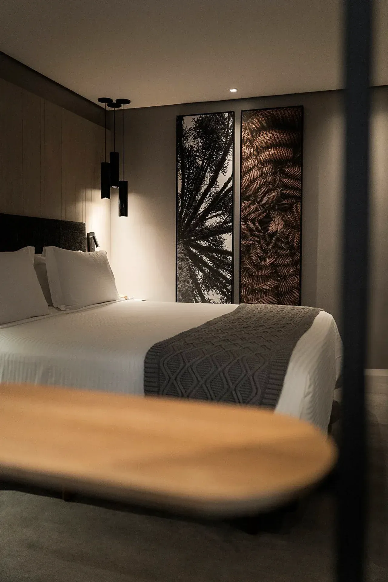 Quarto de hotel moderno e com iluminação suave, cama arrumada e ambiente aconchegante.
