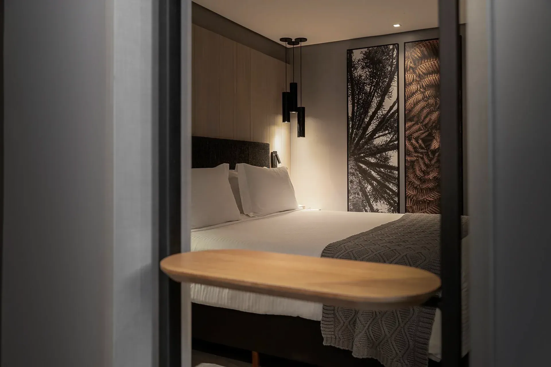 Quarto moderno com cama, cabeceira de madeira e uma pequena mesa redonda em primeiro plano.