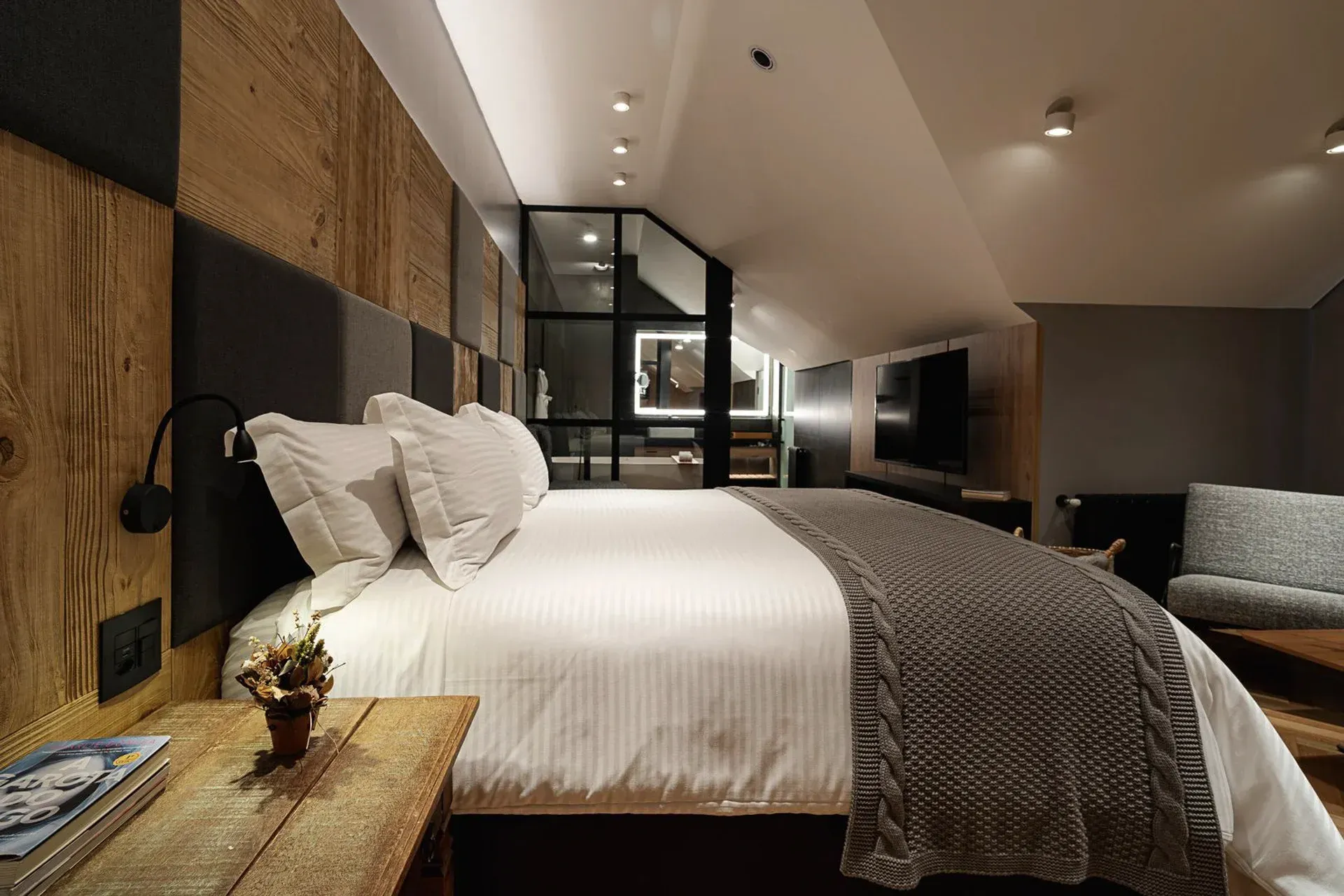 Quarto de hotel moderno com cama grande, paredes revestidas de madeira e área de estar com iluminação suave.