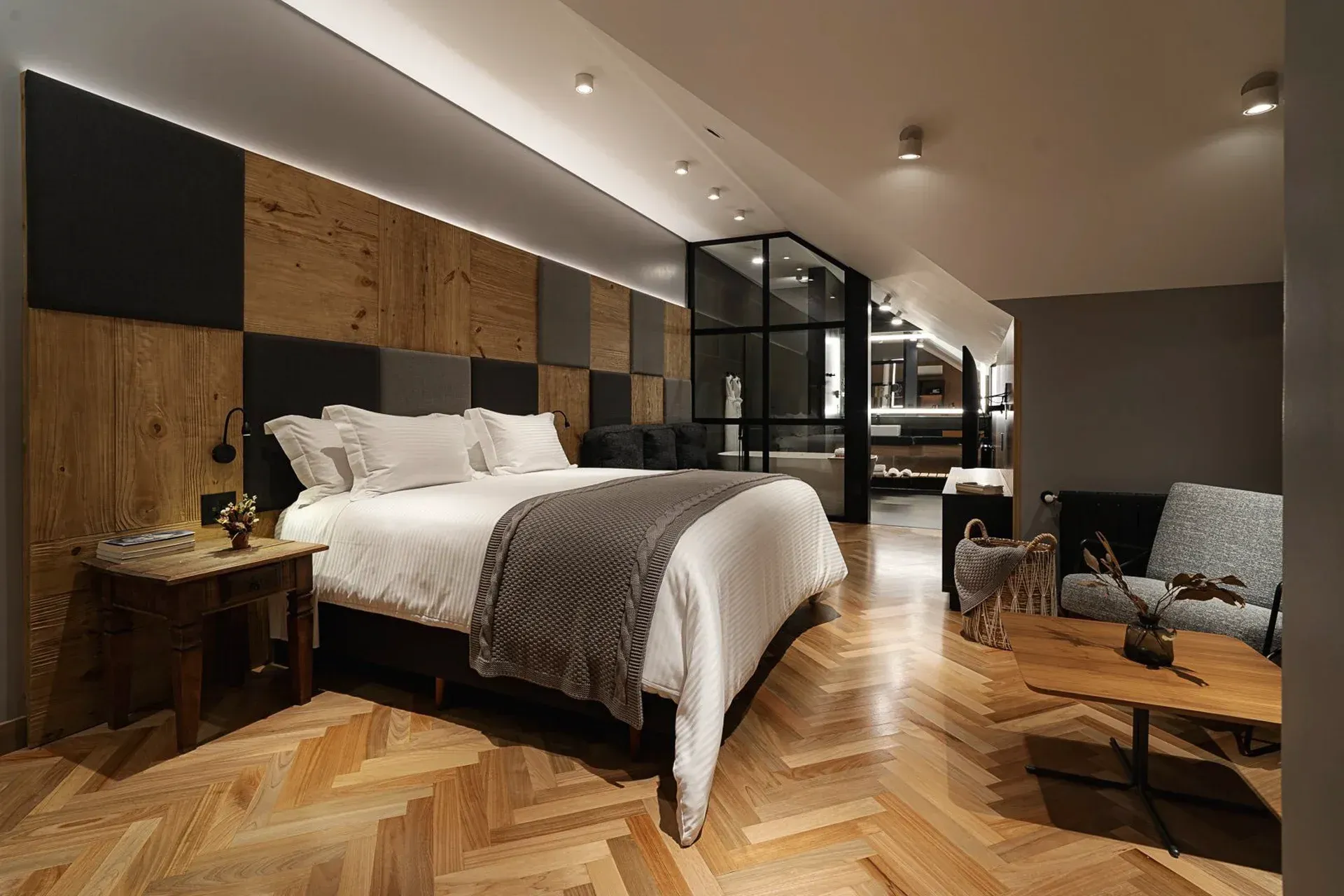 Quarto de hotel moderno com cama grande, piso de madeira aconchegante e área de estar.