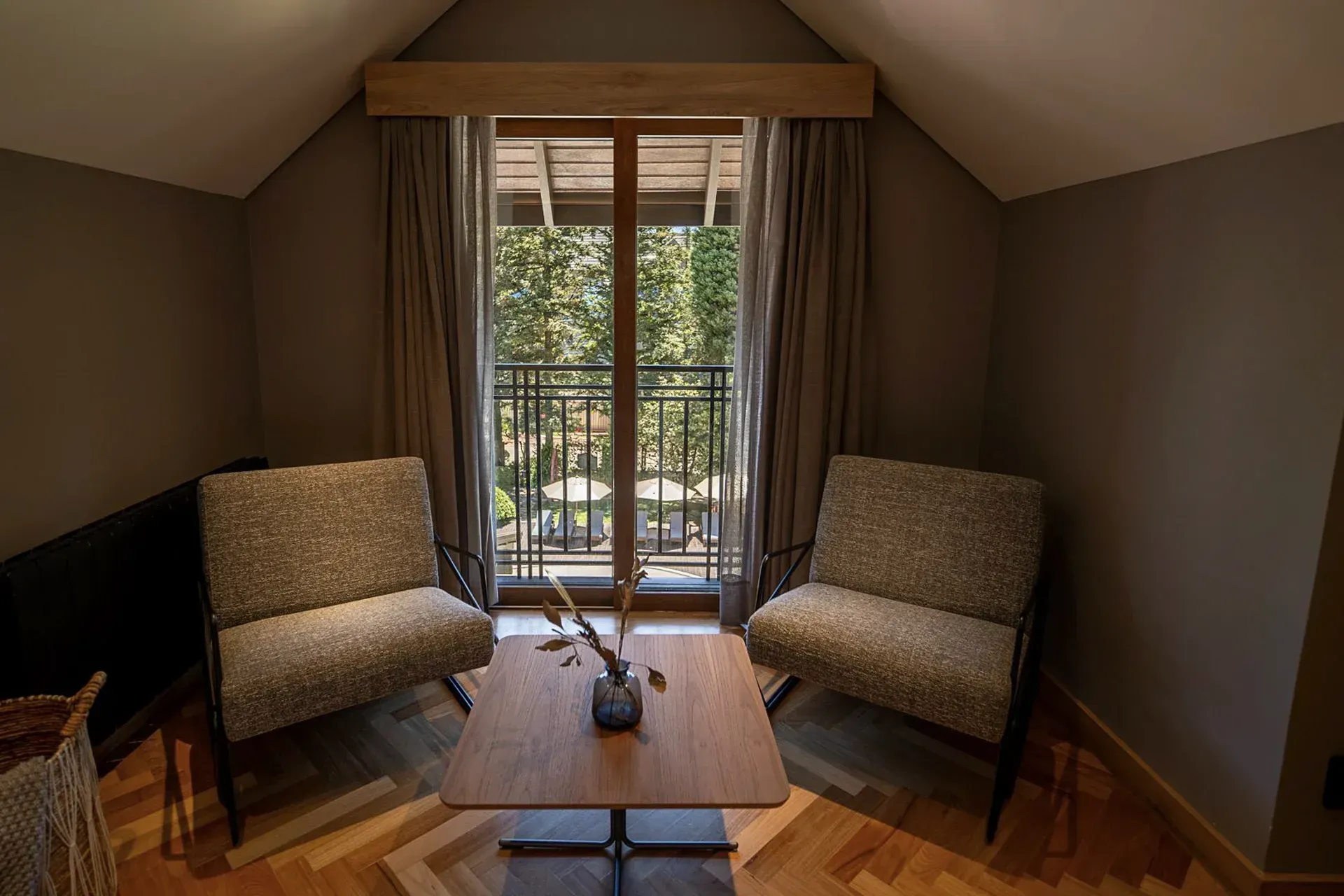 Sala de estar aconchegante com duas cadeiras, uma mesinha e portas de varanda que se abrem para uma área verde.