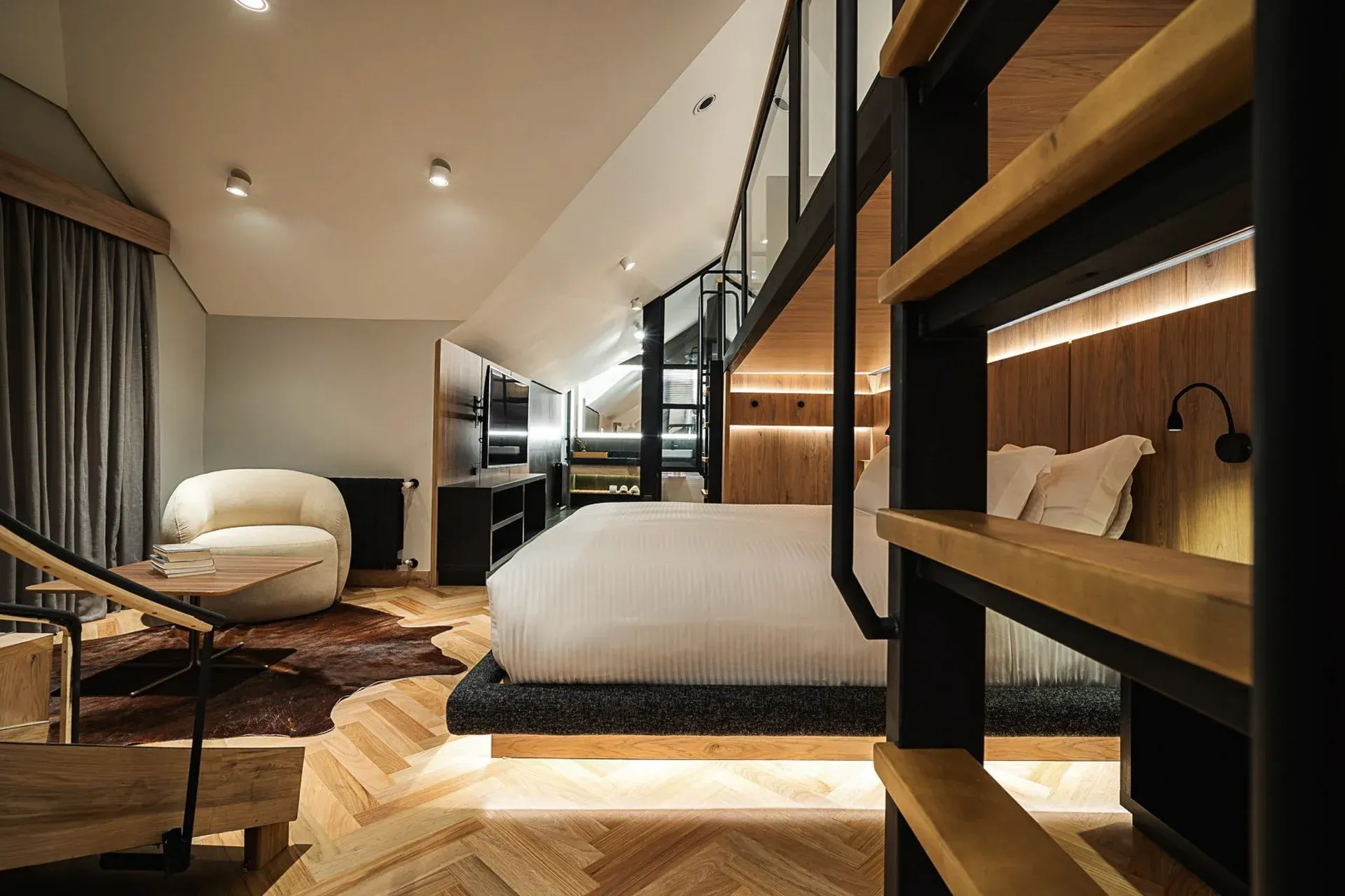 Quarto de hotel moderno com mobiliário de madeira, cama king-size, poltrona e iluminação aconchegante.
