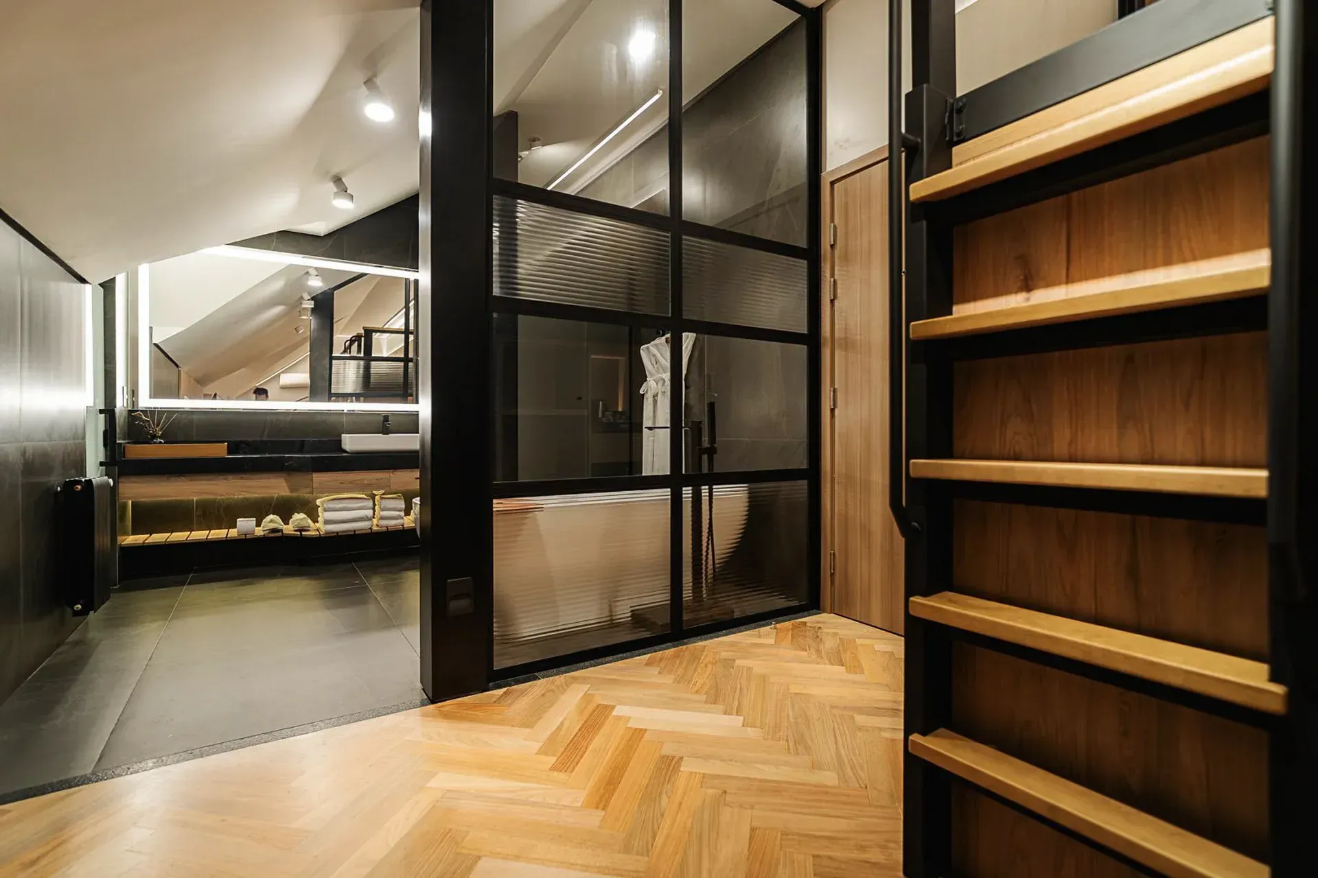 Closet moderno com portas de vidro emolduradas em preto, piso de madeira em espinha de peixe e prateleiras embutidas.