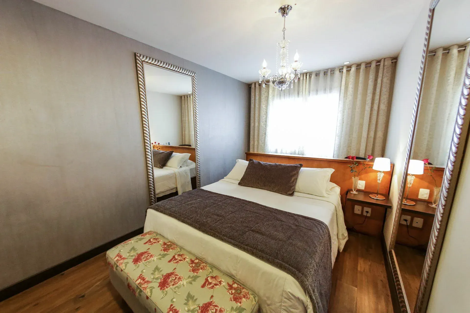 Quarto luminoso com cama arrumada, guarda-roupa com espelho e cortinas na janela, além de abajures.
