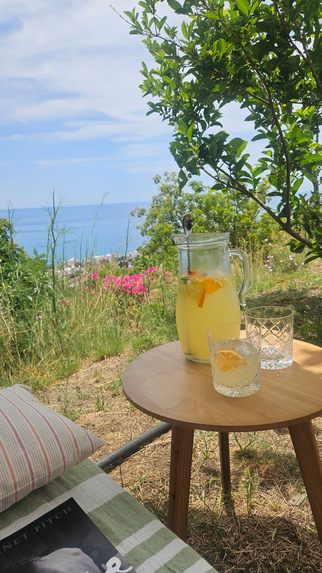 Lemonade on a small table outdoors, ocean view. Clear glass pitcher and cup.