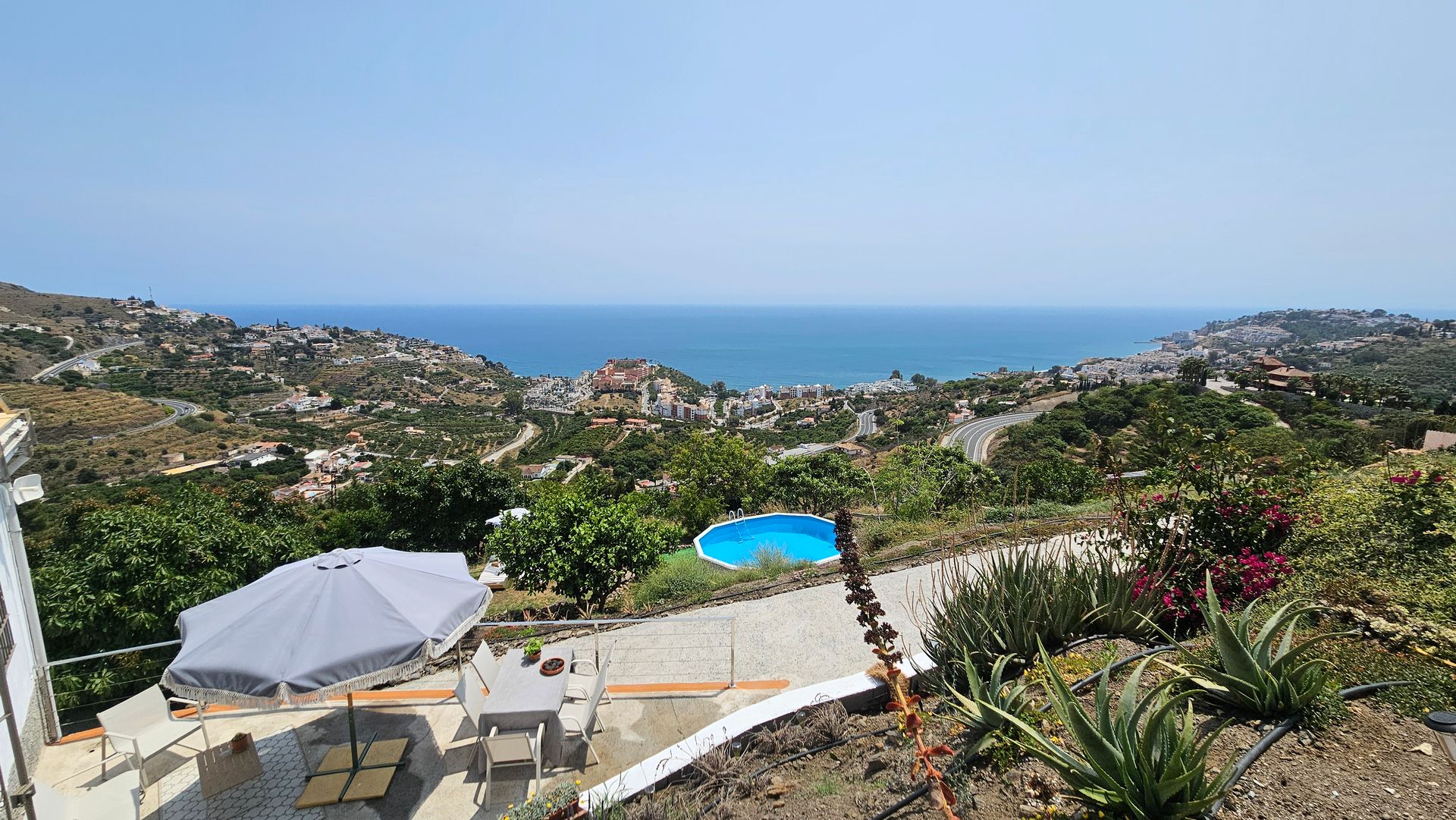 A scenic view of a coastal town with a pool and ocean visible under a clear, blue sky.