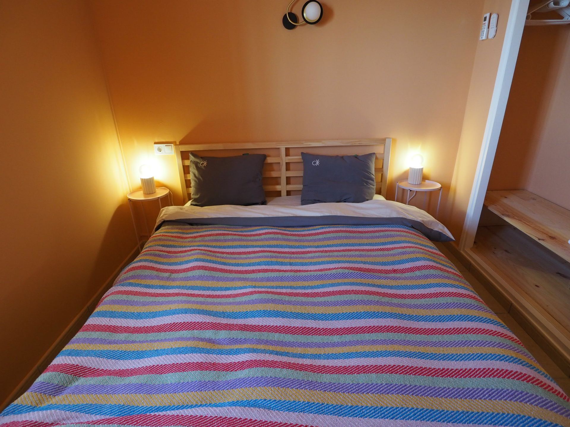 Bedroom with a striped bedspread, two pillows, bedside lamps, and a wooden headboard.