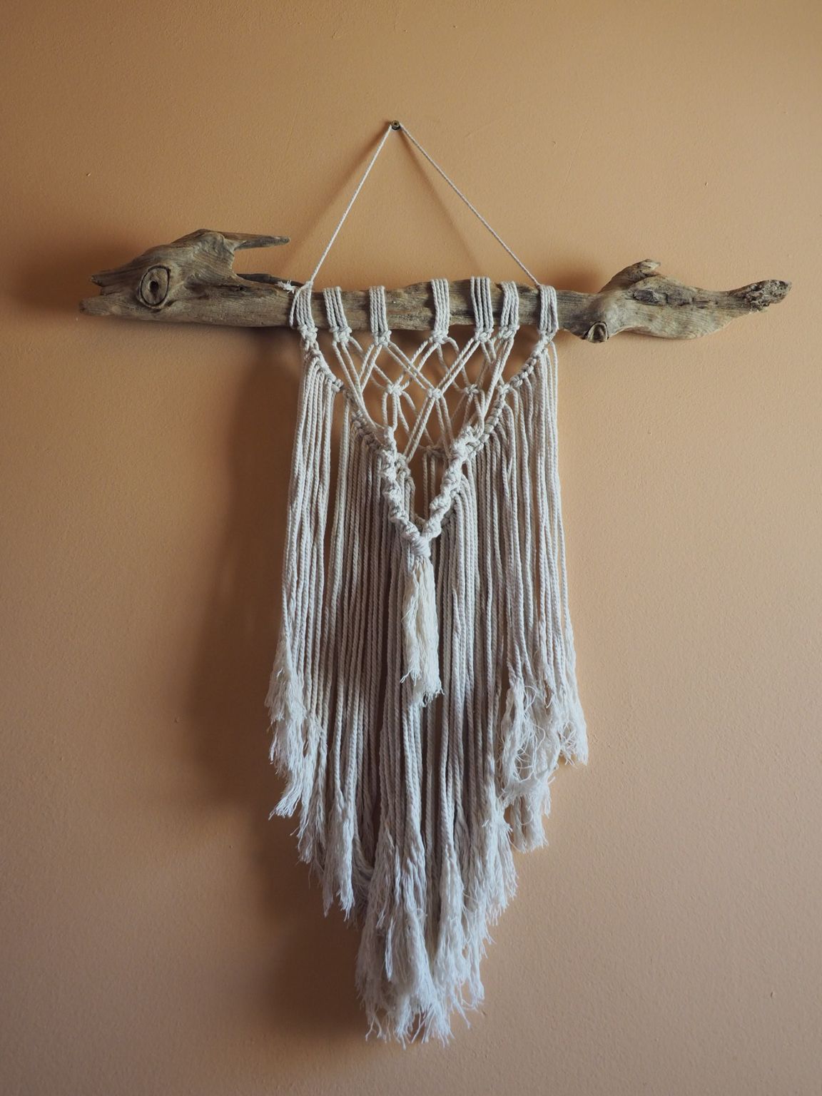 Macrame wall hanging with frayed cotton strands suspended from driftwood branch.