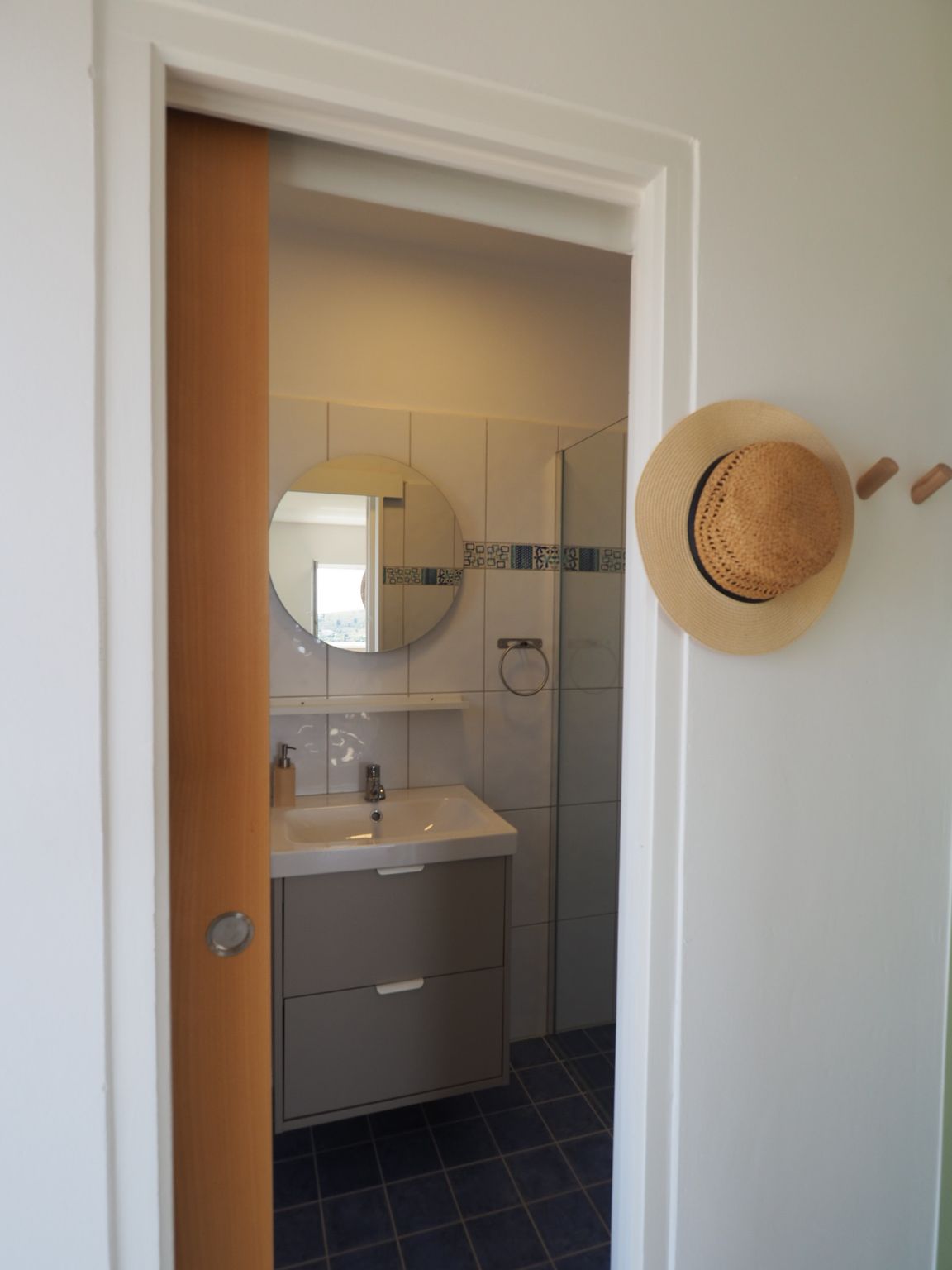 Bathroom doorway with sliding wooden door open; sink, mirror, and hat on wall visible.