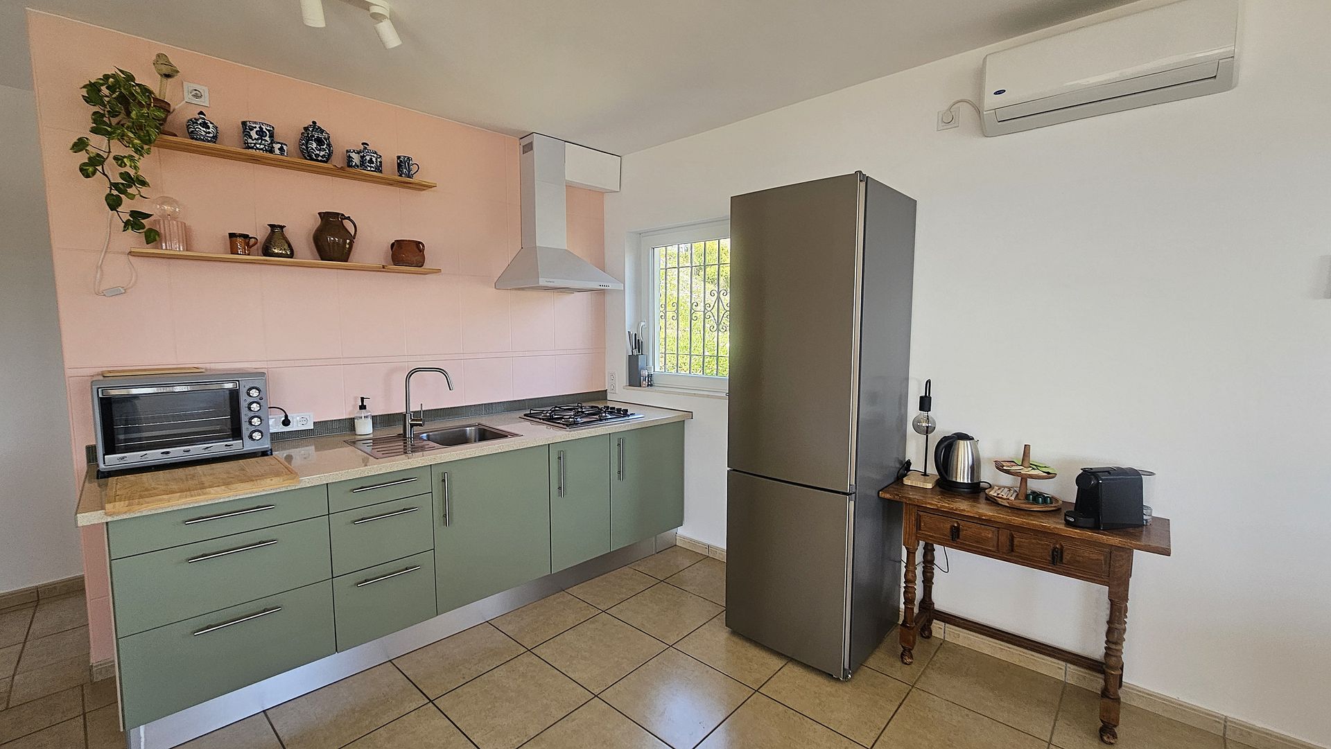 Kitchen with green cabinets, pink wall, and stainless steel refrigerator and appliances.