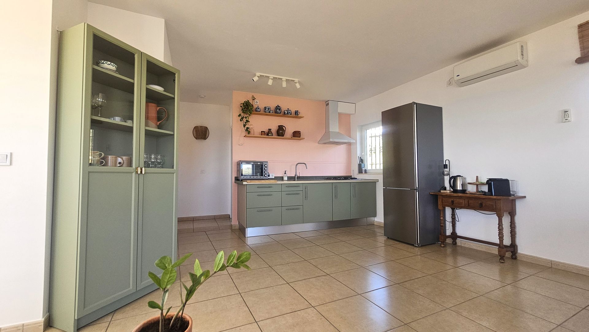 Kitchen with green cabinets, pink accent wall, stainless steel refrigerator, and tiled floor.