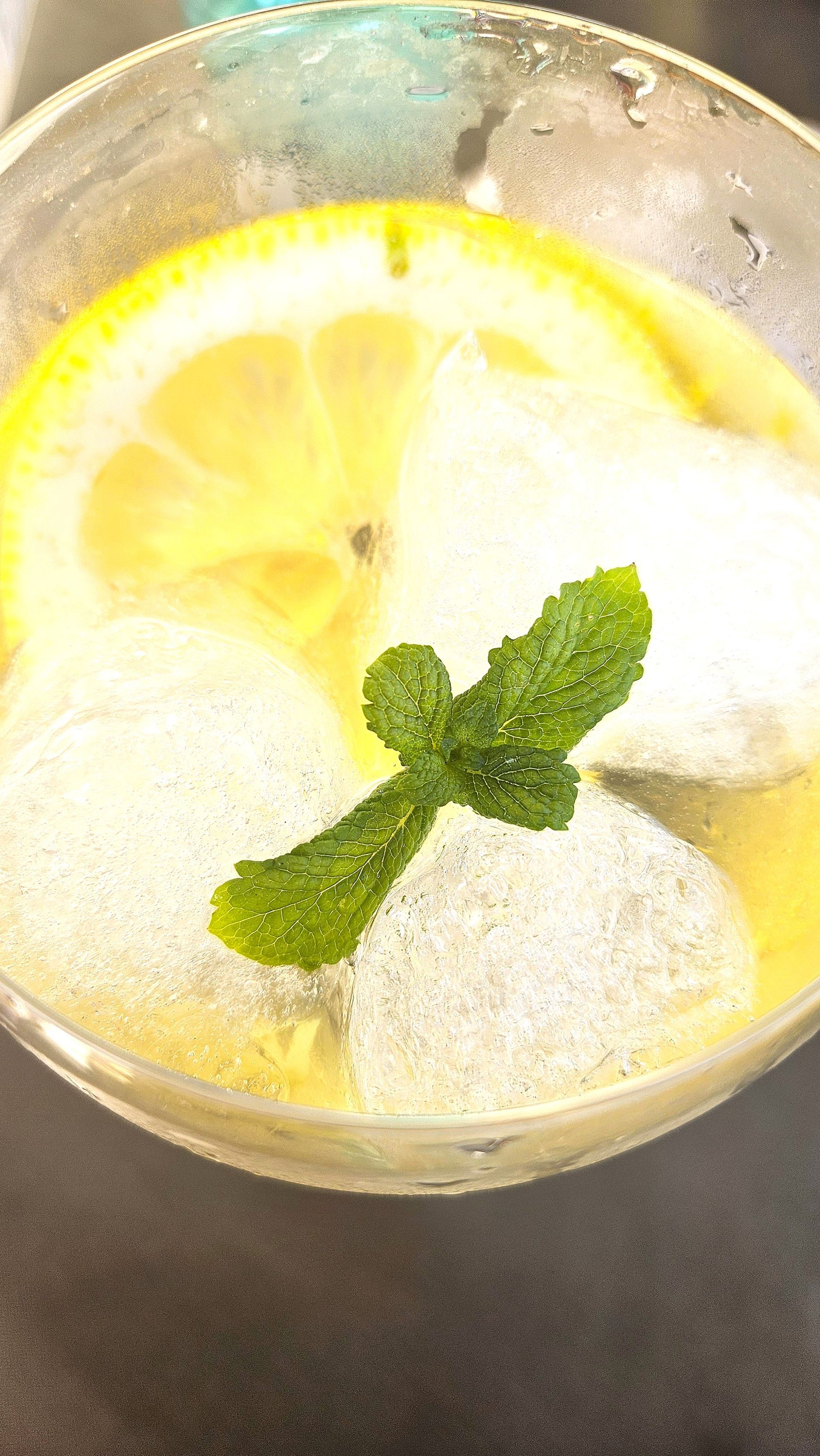 Glass of lemon drink with ice and mint garnish.
