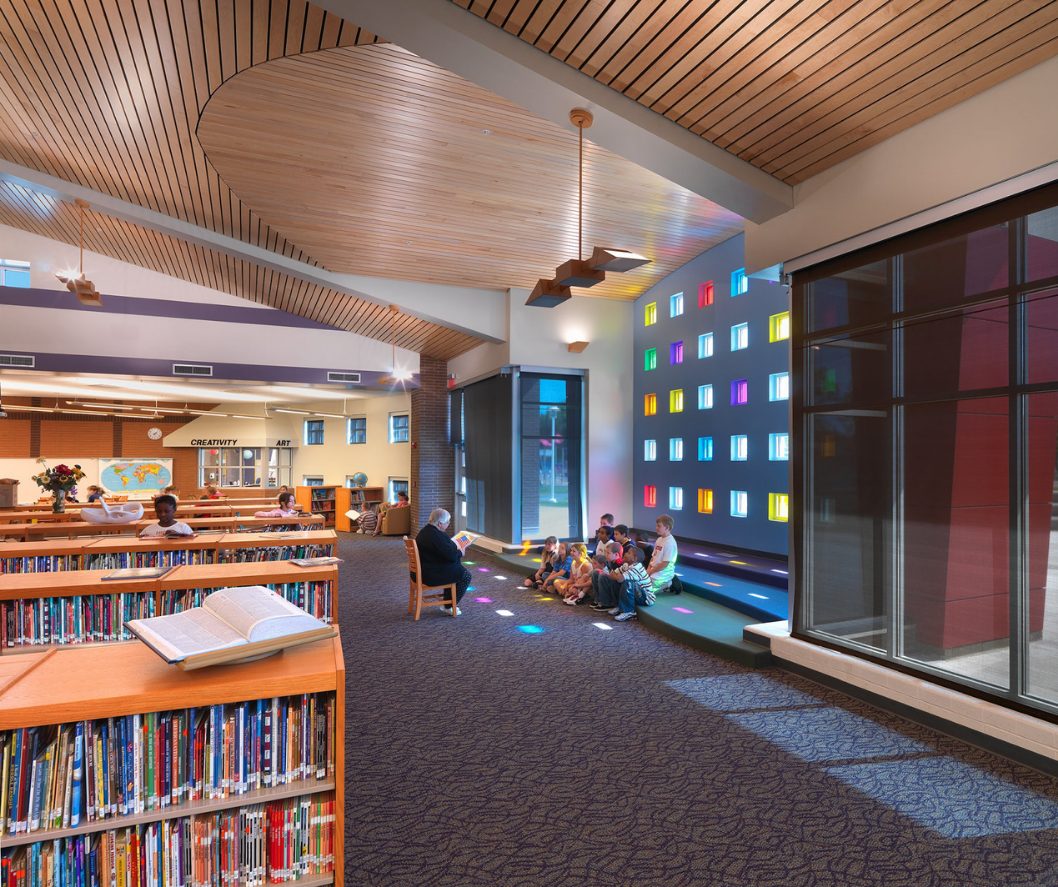 Library interior with bookshelves, colorful light wall, and people reading and sitting.