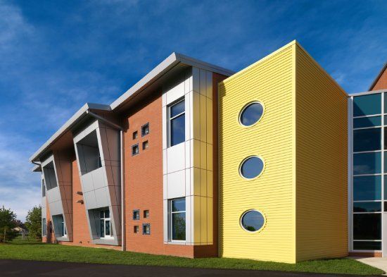 Modern, colorful building with angled walls, yellow tower with porthole windows, blue sky.