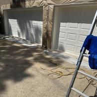 Two white garage doors with brown drop cloths covering the frames, with a ladder and cord in the foreground.