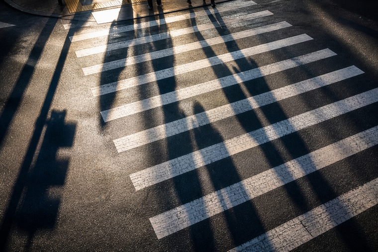 Sunlit crosswalk with long shadows cast across white zebra stripes on dark pavement