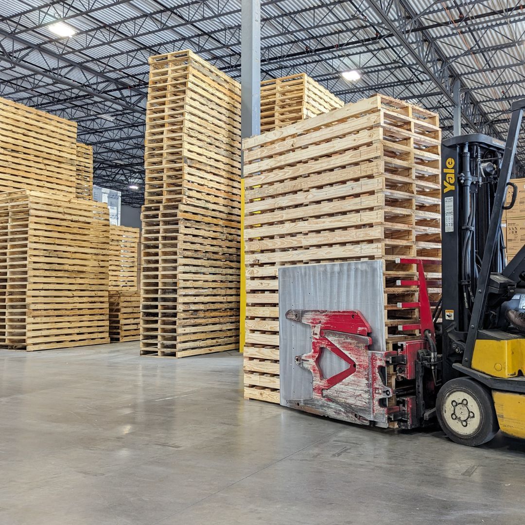Warehouse with stacked wooden pallets and a forklift beside a pallet stack