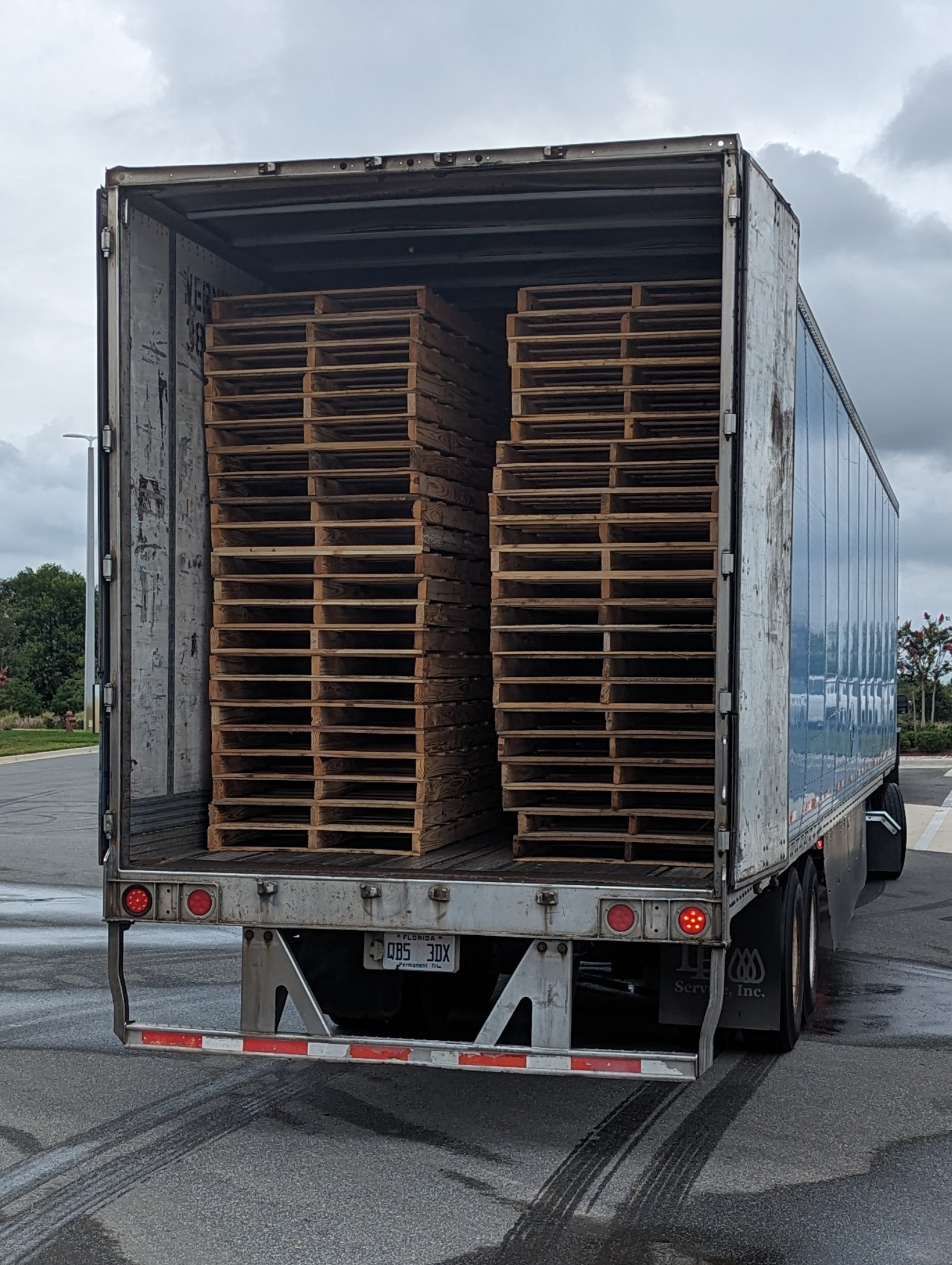 White flatbed truck loaded with stacked wooden pallets parked outdoors on a sunny street