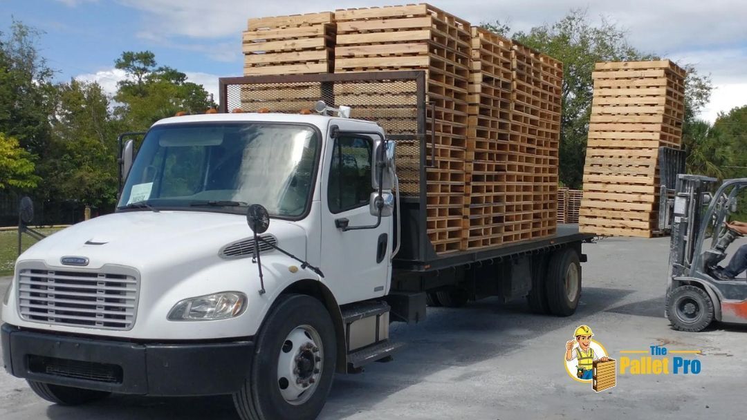 A white truck is loaded with wooden pallets and a forklift is behind it.